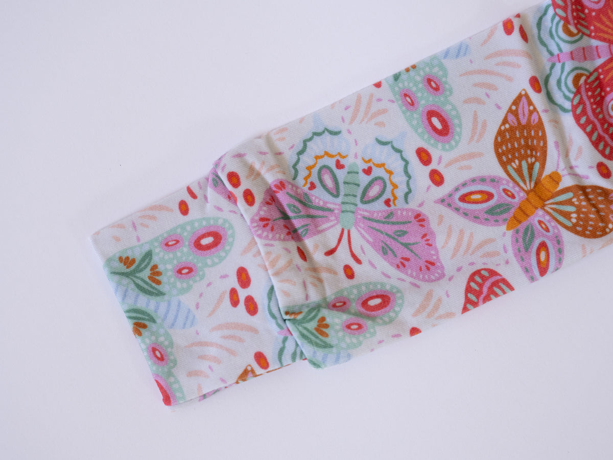 A close-up of a white fabric sleeve or cuff featuring a colorful butterfly and paisley print in pink, orange, green, and red, laid flat on a white background.